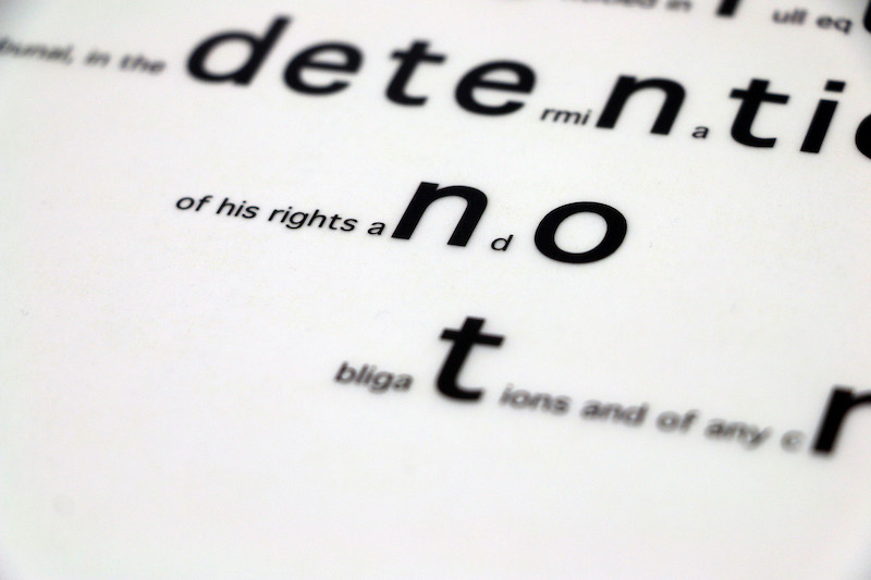 in.definite artwork detail .. a close up of the text in this work ... two sizes of rounded black letters lay on a softened white paper background .. the words read something as one .. but some letters have been enlarged to create contrasting words and meaning .. this snapshot shows us determination ~detention~ of his rights and ~not~ obligations .. the edges of the image and text blur