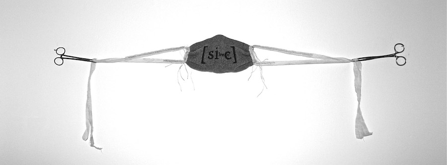blanket silence ..  a black and white image of the artwork displayed outstretched upon a white wall ... a grey woollen face mask has white gauze ties, 2 pulled to each side held by a pair of surgical scissors .. the gauze ties then drape from the scissors grip ... the mask has black text on the front .. [sic] in large letters .. with some smaller indistinguishable letters in between ... pale threads of various lengths drape down from where the ties have been hand-sewn to the side of the mask .. the four fabric ties are each greyed near the mask .. from text perhaps? 
